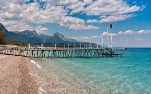 Small wooden pier on shingle beach and aquamarine water in popul